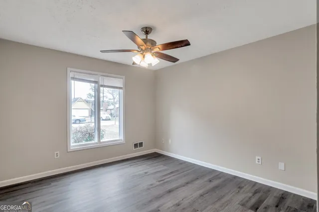 an empty room with wooden floor chandelier fan and windows