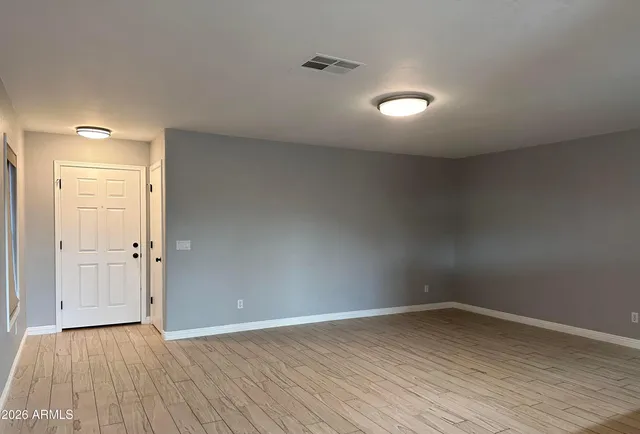 a view of an empty room with wooden floor and a kitchen