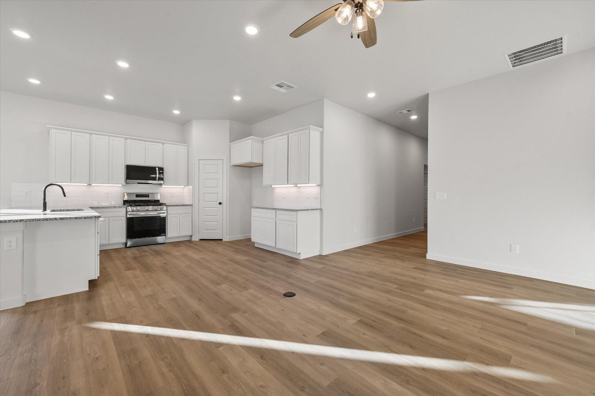 7007 56th Street Lubbock, TX 79407 - Photo 6 of 22 a kitchen with granite countertop a refrigerator oven a sink and white cabinets with wooden floor next to windows