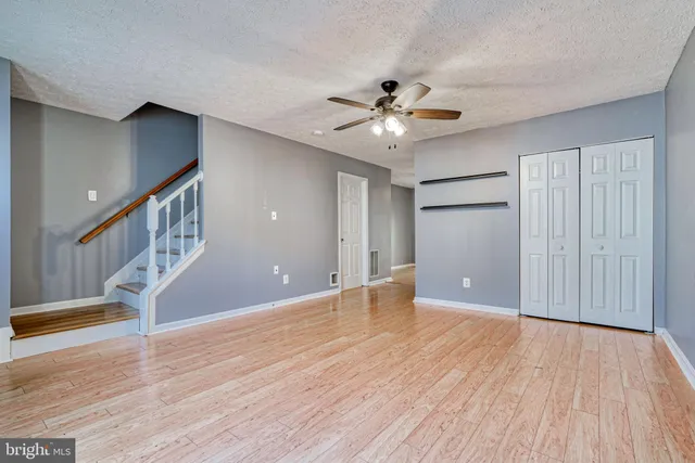 a view of an empty room with wooden floor and a ceiling fan