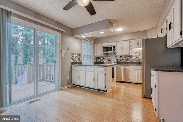 a kitchen with stainless steel appliances granite countertop a refrigerator a stove top oven a sink with wooden floors and white cabinets