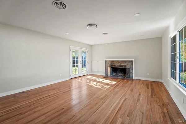 a view of an empty room with wooden floor fireplace and a window