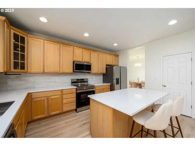 a kitchen with stainless steel appliances granite countertop a sink a stove a refrigerator cabinets and a dining table