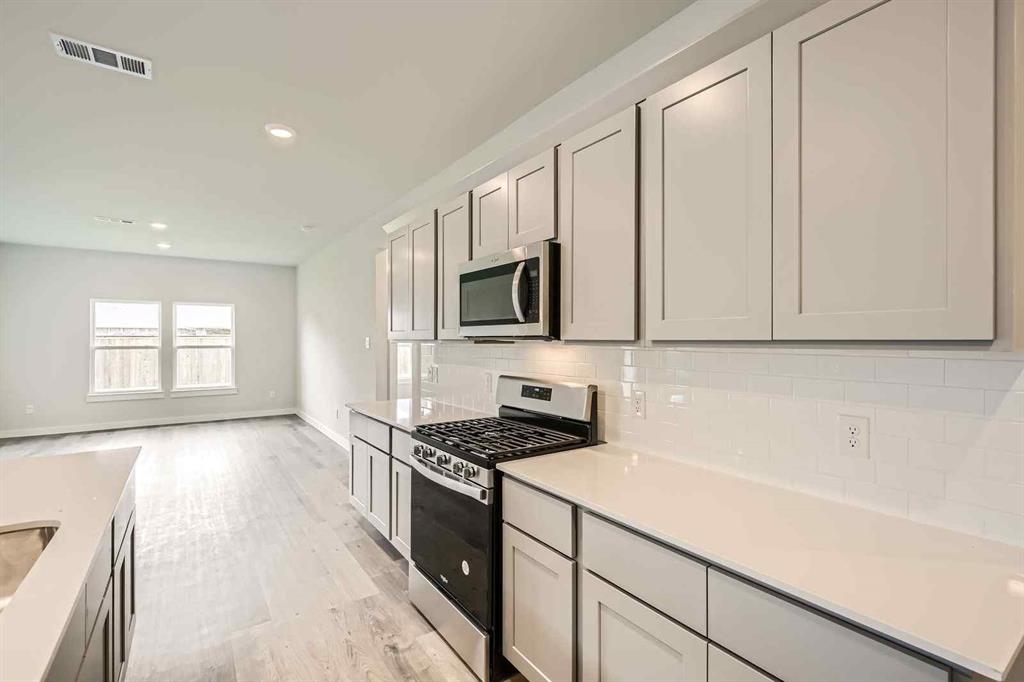 736 Vineyard Way Forney, TX 75126 - Photo 7 of 40 a kitchen with granite countertop a stove a sink and a white cabinets