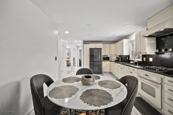 a kitchen with stainless steel appliances granite countertop a dining table chairs and refrigerator