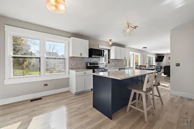 a kitchen with stainless steel appliances granite countertop a stove top oven a sink dishwasher a refrigerator and white cabinets with wooden floor