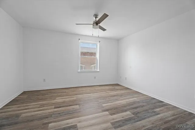 an empty room with wooden floor ceiling fan and windows