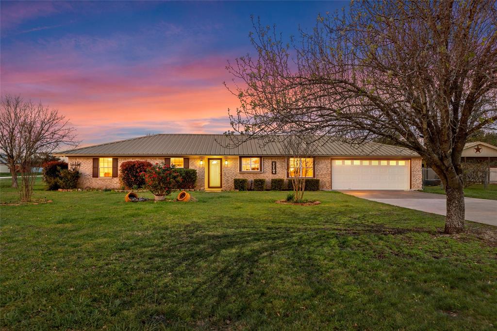 Single story home featuring driveway, a yard, brick siding, and an attached garage