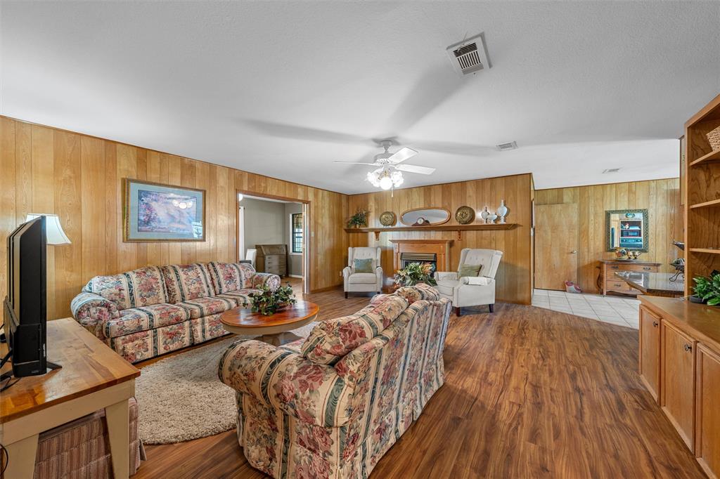 117 North 9th Street Lott, TX 76656 - Photo 3 of 28 Living area with a fireplace, dark wood finished floors, ceiling fan, and wooden walls