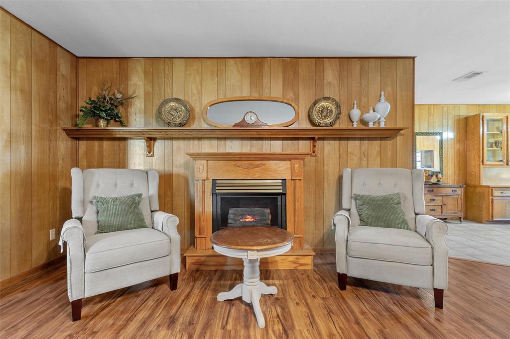 117 North 9th Street Lott, TX 76656 - Photo 4 of 28 Sitting room with a glass covered fireplace, wood walls, and wood finished floors