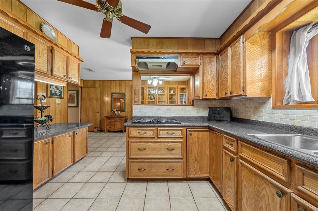 117 North 9th Street Lott, TX 76656 - Photo 6 of 28 Kitchen with wood finish cabinets, dark countertops, light tile patterned floors, black appliances, and decorative backsplash