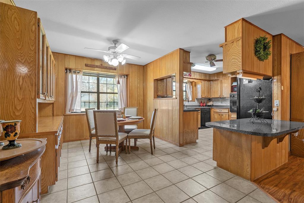 117 North 9th Street Lott, TX 76656 - Photo 7 of 28 Kitchen featuring ceiling fan, black appliances, light tile patterned floors, wood walls, and a breakfast bar