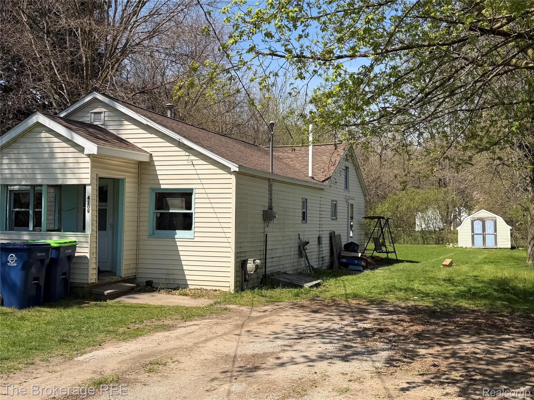 4209 Williamson Road Saginaw, MI 48601 - Photo 1 of 5 View of property exterior featuring a yard, a storage unit, a shingled roof, and view of scattered trees