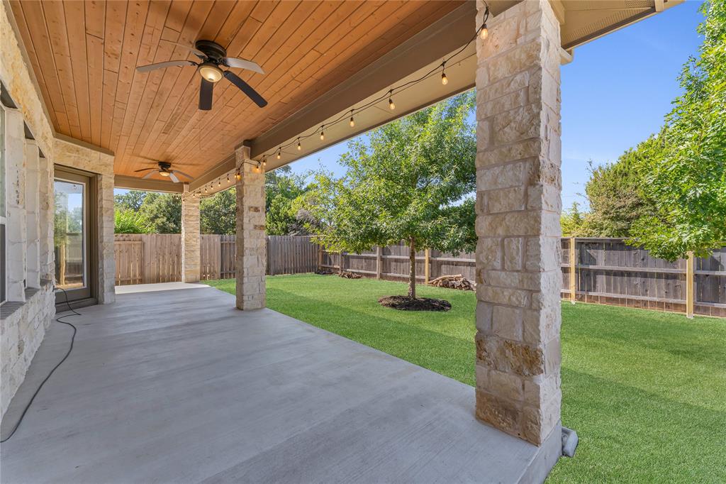 110 Magona Trail Georgetown, TX 78628 - Photo 35 of 38 An inviting covered patio with stone pillars overlooks a verdant, fenced backyard.