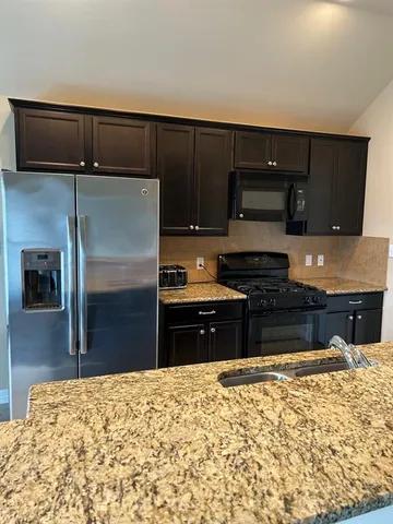 a kitchen with granite countertop a refrigerator and a stove top oven