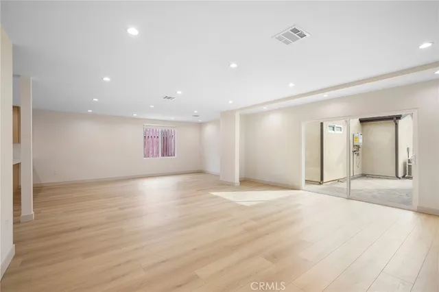a view of an empty room with wooden floor and kitchen space