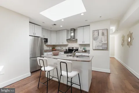 a kitchen with stainless steel appliances granite countertop a dining table chairs refrigerator and sink