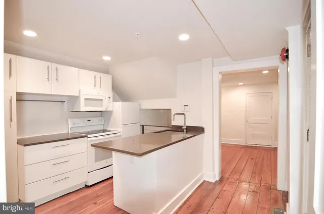 a kitchen with kitchen island a sink stove and white cabinets with wooden floor