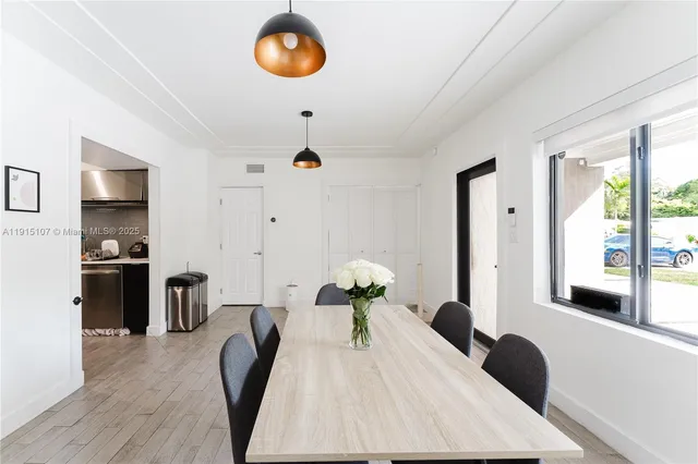 a white kitchen with stainless steel appliances granite countertop a stove a refrigerator a sink a dining table and chairs with wooden floor