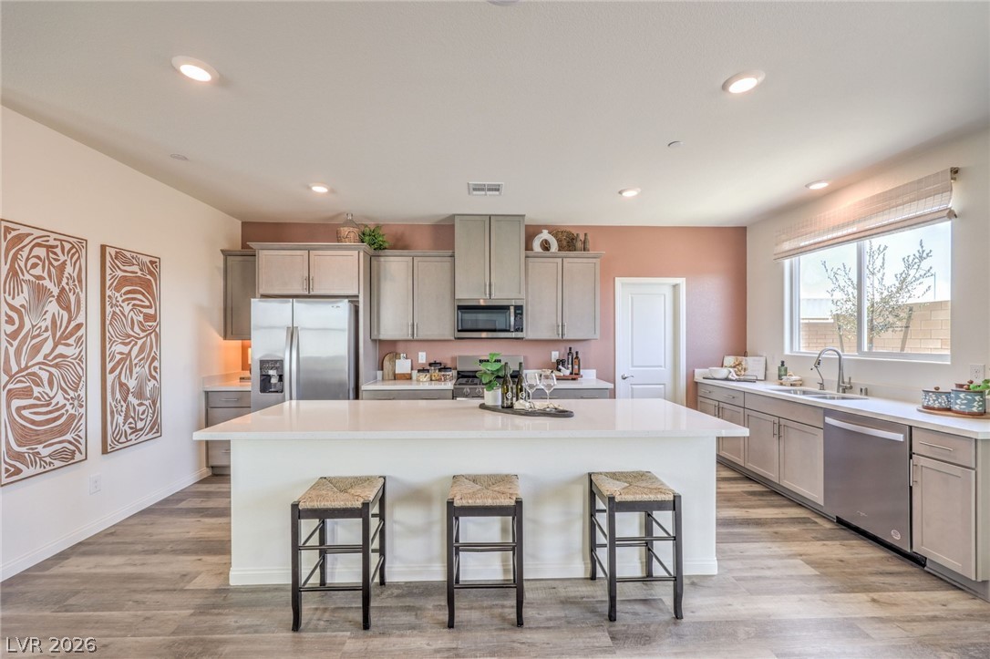 1017 Copper Robin Street Henderson, NV 89011 - Photo 13 of 43 Kitchen featuring appliances with stainless steel finishes, a sink, gray cabinetry, a kitchen breakfast bar, and recessed lighting. Photo is representational only; actual home finishes may vary.