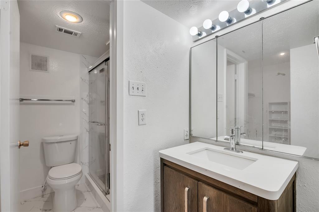 4525 North O'Connor Road, Unit 1184 Irving, TX 75062 - Photo 15 of 20 The bathroom features a vanity with a white countertop and a chrome faucet, a mirrored medicine cabinet with overhead lighting, and a glass-enclosed shower with white tiled walls