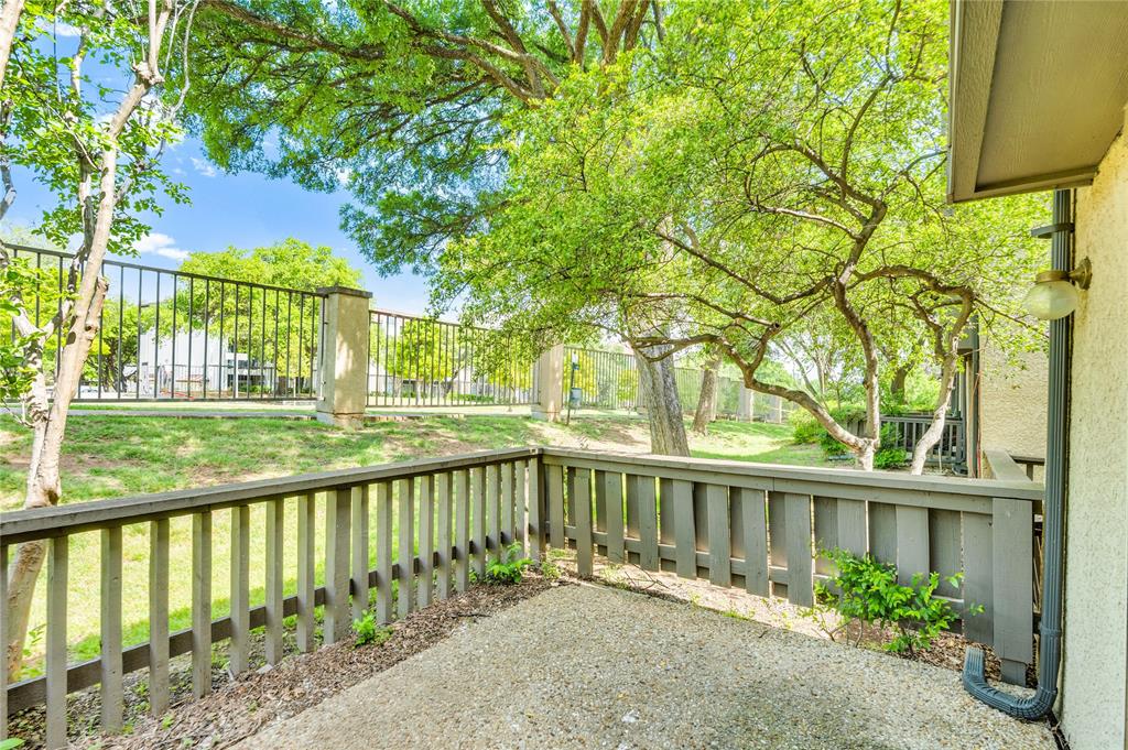 4525 North O'Connor Road, Unit 1184 Irving, TX 75062 - Photo 18 of 20 This property features an exterior patio with a railing, overlooking a verdant lawn with mature trees, and a black wrought-iron fence