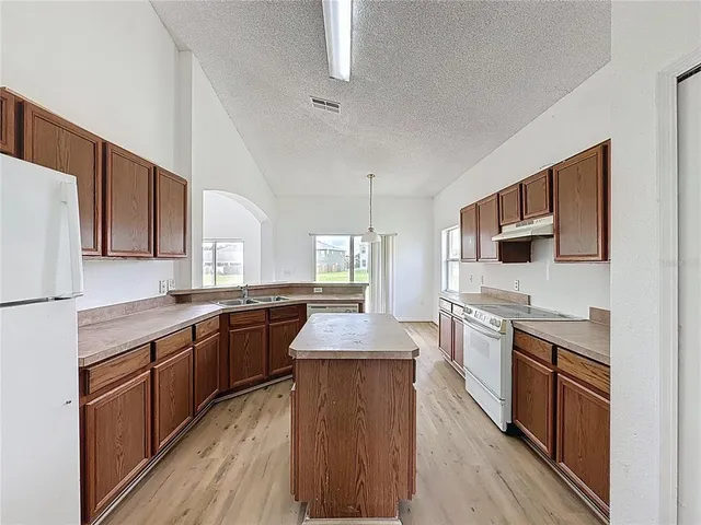 a kitchen with stainless steel appliances granite countertop wooden cabinets a refrigerator a stove a sink and a oven with wooden floors