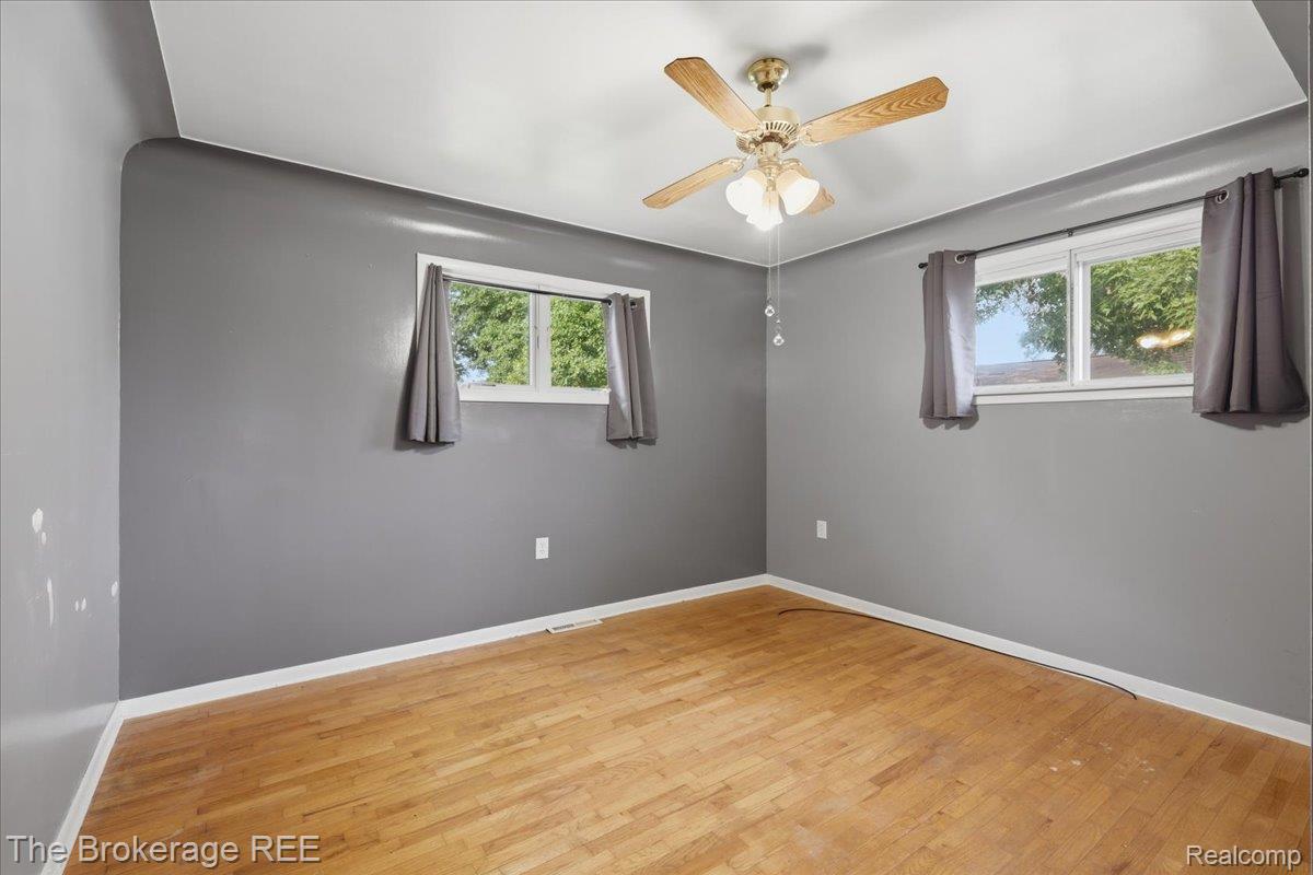 11973 East Brooks Road Lennon, MI 48449 - Photo 22 of 28 Hardwood flooring, two windows with white trim, ceiling fan light fixture, and neutral gray walls
