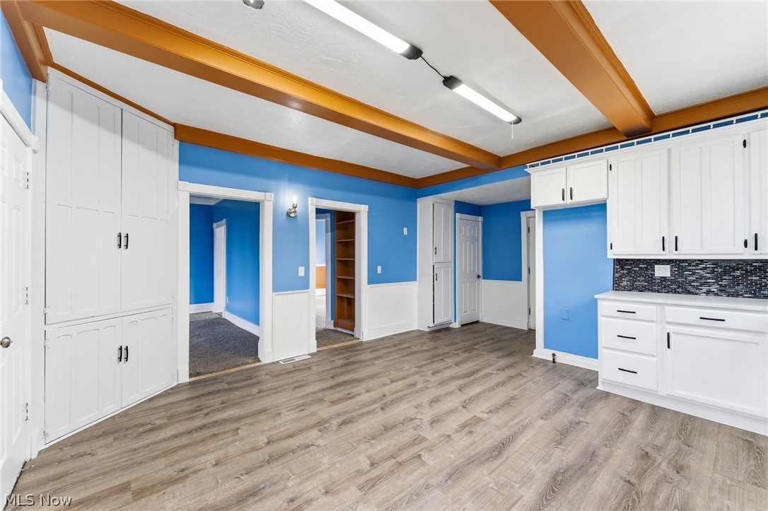 563 Geneva Avenue Struthers, OH 44471 - Photo 7 of 31 Kitchen with light wood-type flooring, white cabinetry, beamed ceiling, light countertops, and wainscoting