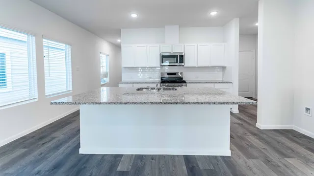 a kitchen with kitchen island granite countertop a stove a sink and white cabinets with wooden floor