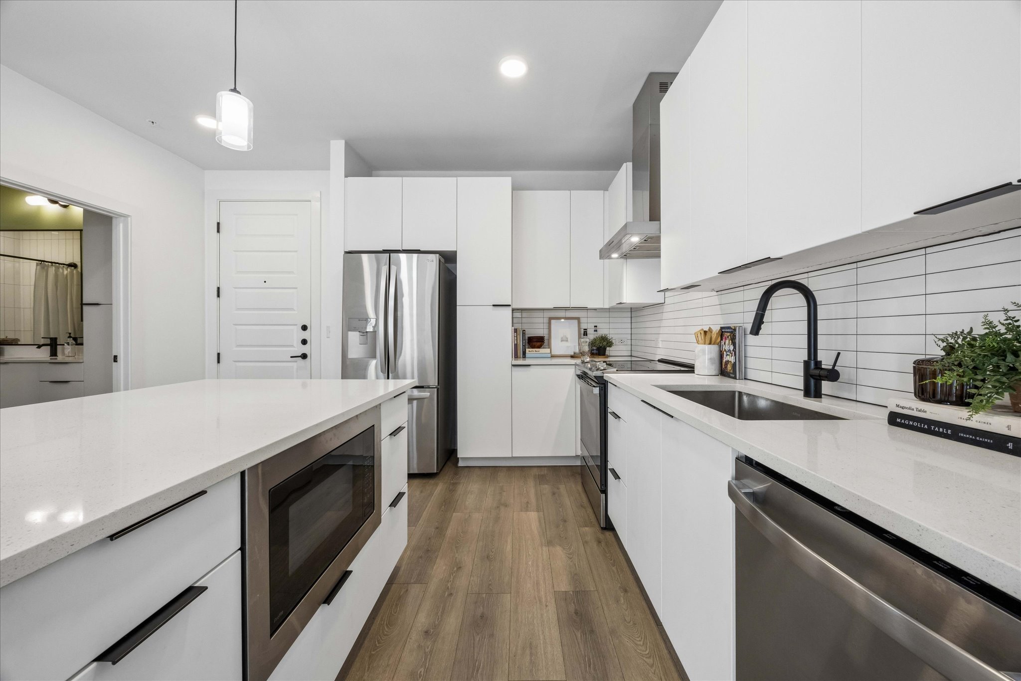 2220 Webberville Road, Unit 216 Austin, TX 78702 - Photo 8 of 26 Modern kitchen featuring white cabinetry, light-toned countertops, wood-finish flooring, stainless steel appliances, and a subway tile backsplash