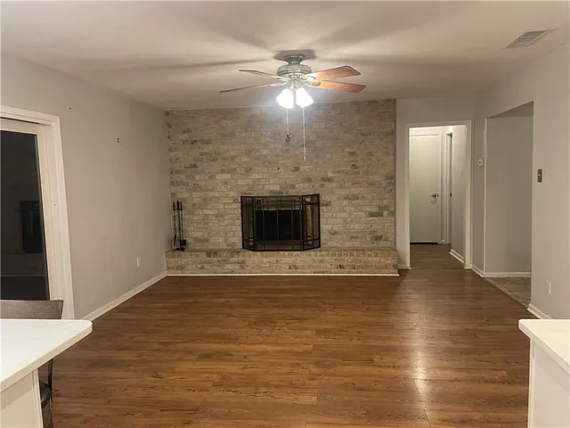 a view of a livingroom with a fireplace a ceiling fan and wooden floor