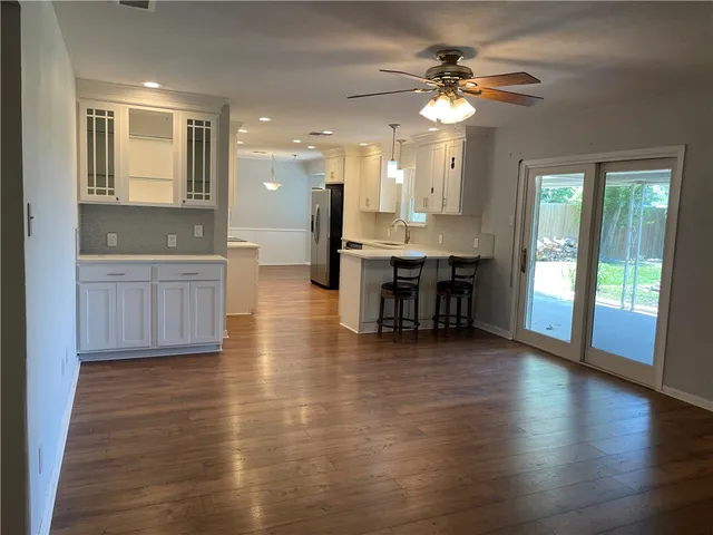 a view of an empty room and kitchen with wooden floor