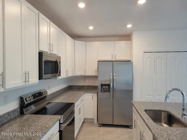 a kitchen with stainless steel appliances granite countertop a refrigerator a stove a sink a microwave a refrigerator and white cabinets with wooden floor