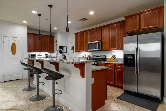 a kitchen with stainless steel appliances granite countertop a refrigerator a stove a sink a dining table and chairs with wooden floor