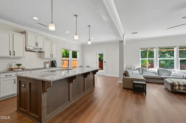 an open kitchen with granite countertop a stove and white cabinets with wooden floor