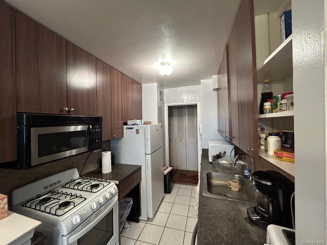 17-85 215th Street, Unit 1R Queens, NY 11360 - Photo 24 of 33 Kitchen with wooden walls, white appliances, sink, and light tile patterned floors