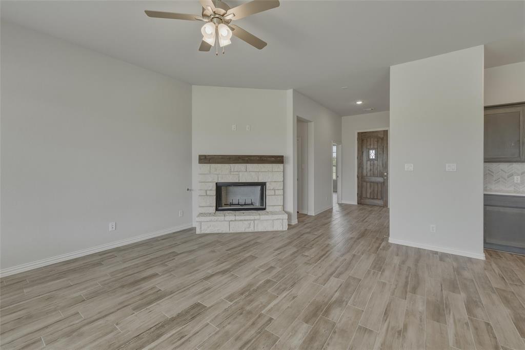 131 Big Sky Road Decatur, TX 76234 - Photo 9 of 23 Living area featuring wood-finish flooring, a ceiling fan, a fireplace with stone surround and wood mantel, and a dark wood entry door