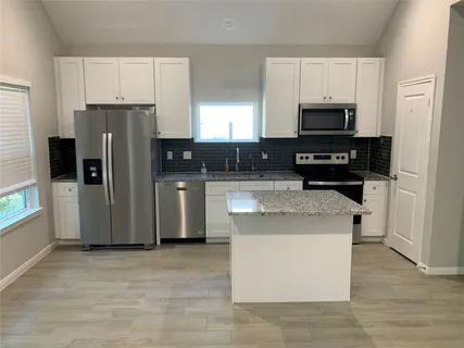 a kitchen with stainless steel appliances granite countertop a stove top oven a refrigerator a sink and dishwasher with white cabinets