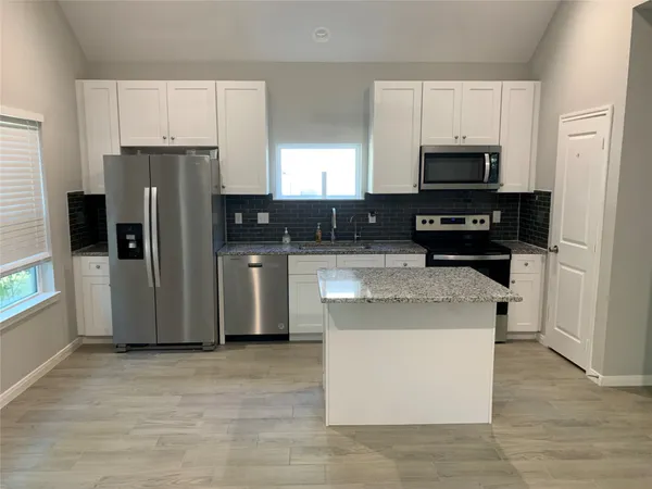 a kitchen with stainless steel appliances granite countertop a stove top oven a refrigerator a sink and dishwasher with white cabinets