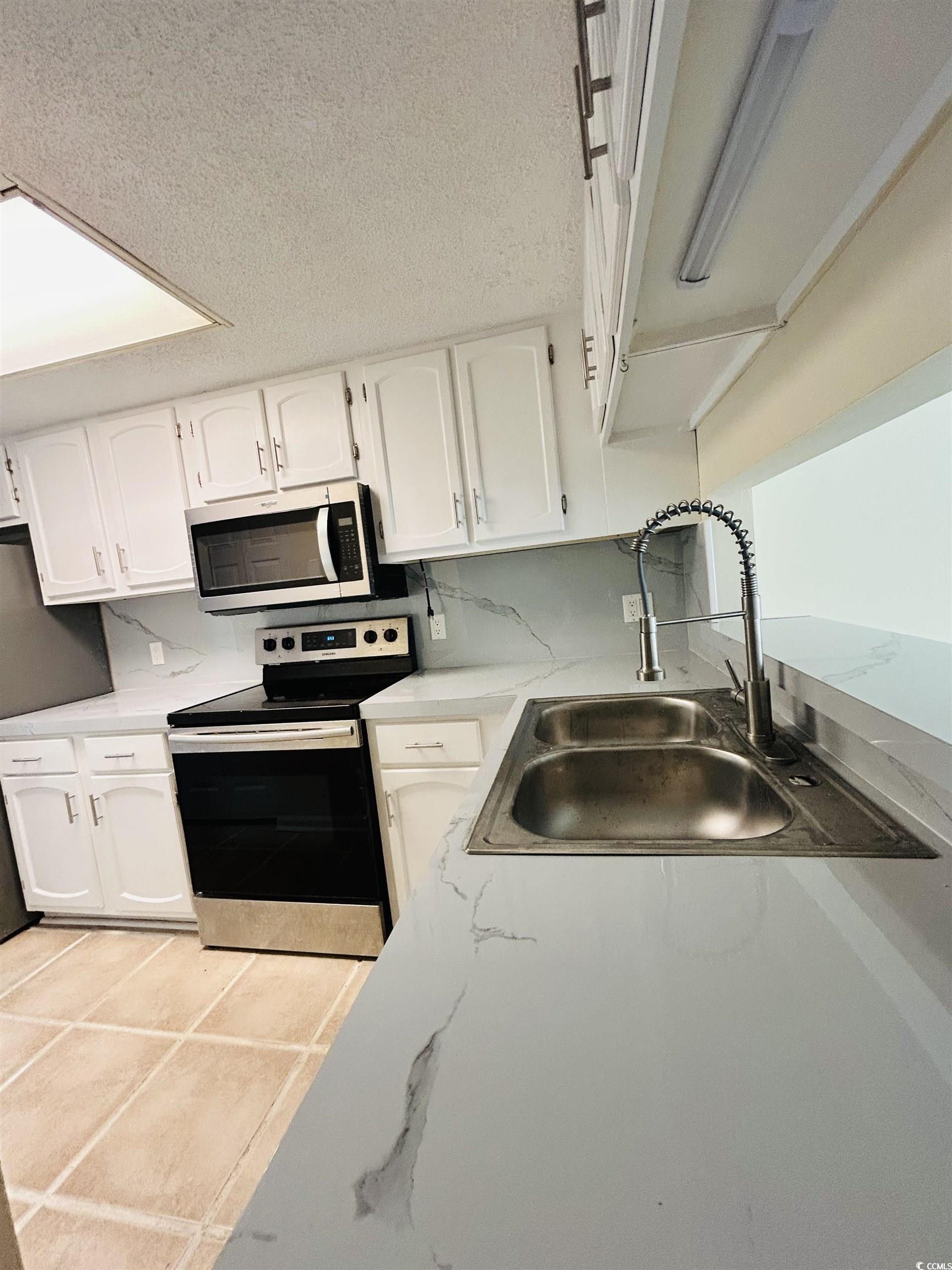 306 76th Avenue North, Unit B2 Myrtle Beach, SC 29572 - Photo 2 of 6 Kitchen featuring white cabinetry, appliances with stainless steel finishes, a textured ceiling, light tile patterned floors, and light countertops