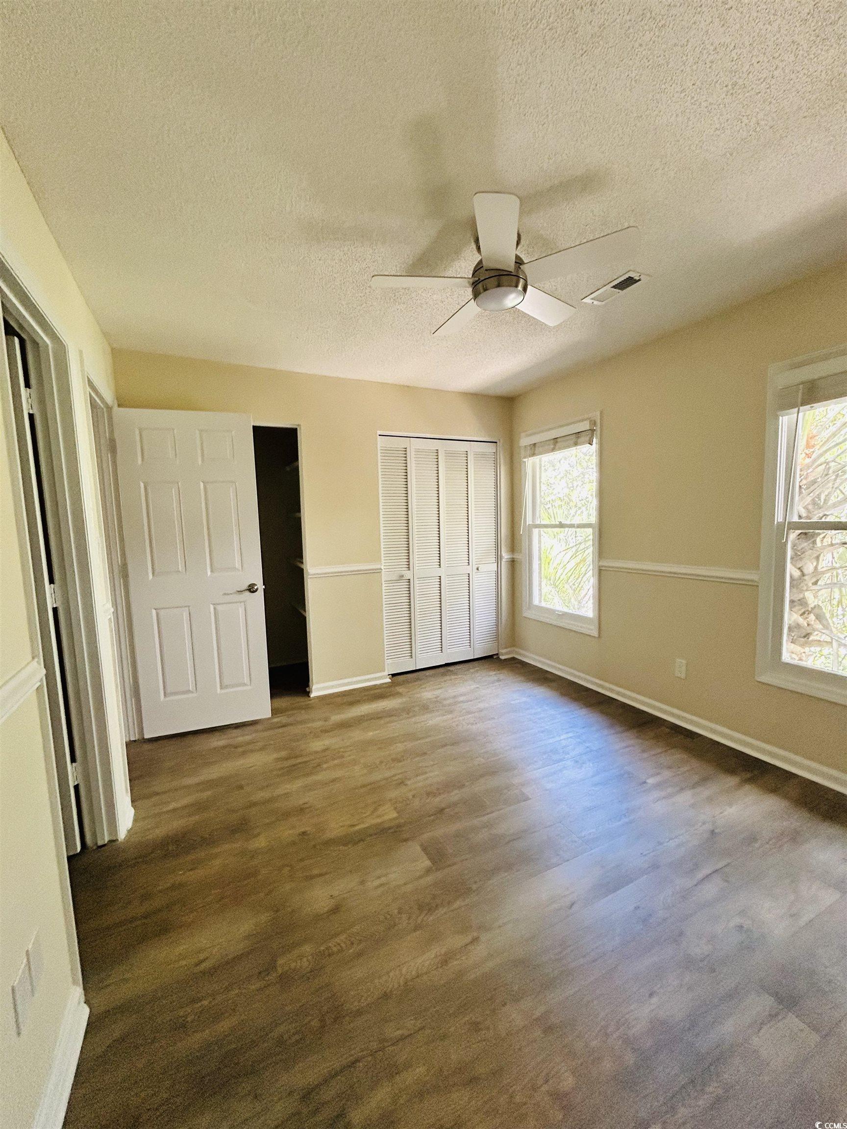 306 76th Avenue North, Unit B2 Myrtle Beach, SC 29572 - Photo 4 of 6 Unfurnished bedroom featuring multiple windows, wood finished floors, a textured ceiling, a closet, and ceiling fan