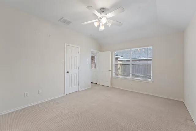 an empty room with chandelier fan and windows