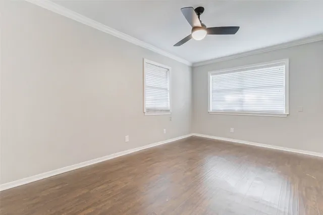 an empty room with wooden floor ceiling fan and windows