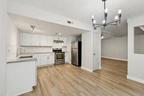 a kitchen with stainless steel appliances granite countertop a refrigerator a sink dishwasher a stove and white countertops with wooden floor