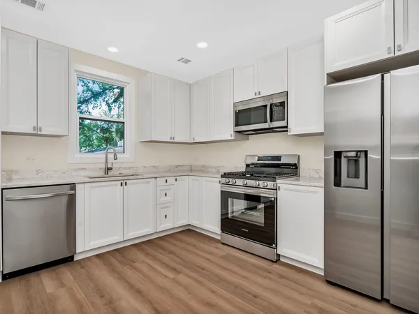 a kitchen with stainless steel appliances white cabinets a sink a stove a microwave and wooden floors