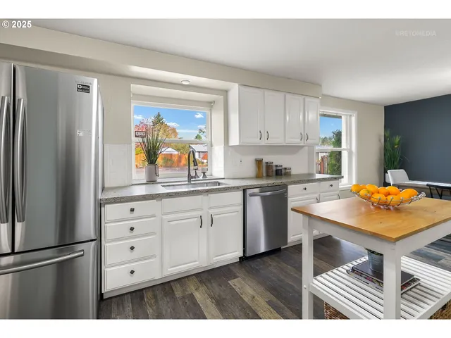 a kitchen with stainless steel appliances granite countertop a refrigerator a stove a sink and white cabinets with wooden floor