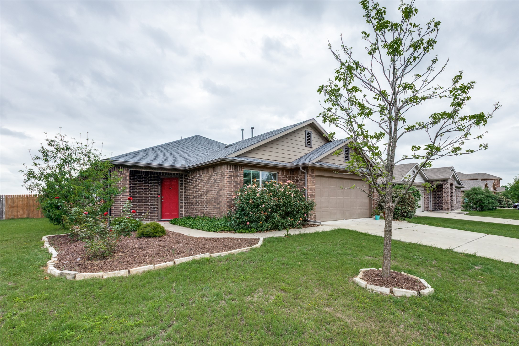 2909 Centrum Drive Austin, TX 78754 - Photo 4 of 30 The property presents a brick exterior with a red front door, an attached garage, and a well-maintained lawn