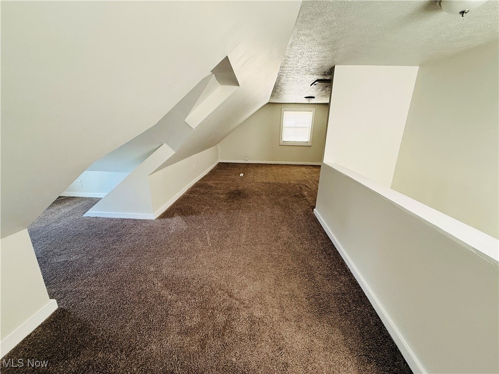 5239 Arch Street Maple Heights, OH 44137 - Photo 10 of 25 Additional living space featuring dark colored carpet, a textured ceiling, and lofted ceiling