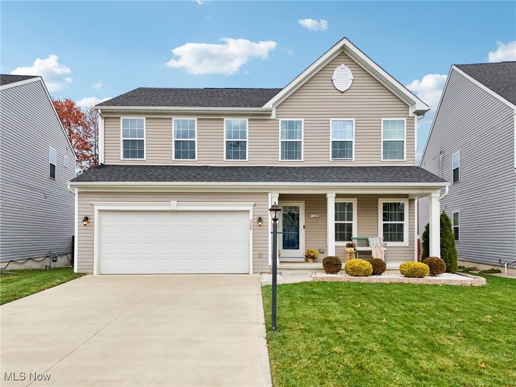 Traditional-style home featuring covered porch, concrete driveway, a garage, a front lawn, and a shingled roof